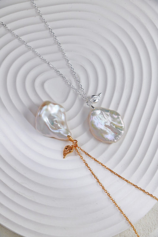 Two elegant pearls on a white plate, accompanied by delicate chain necklaces, available in Silver and Gold.