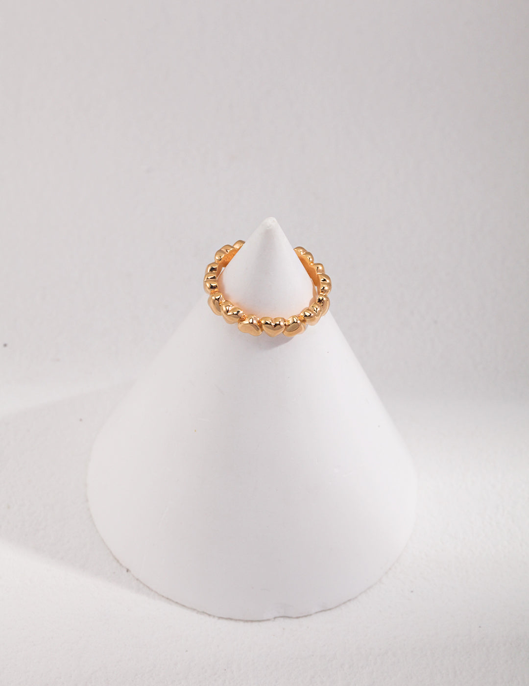 A gold hearts ring placed on a white cone.