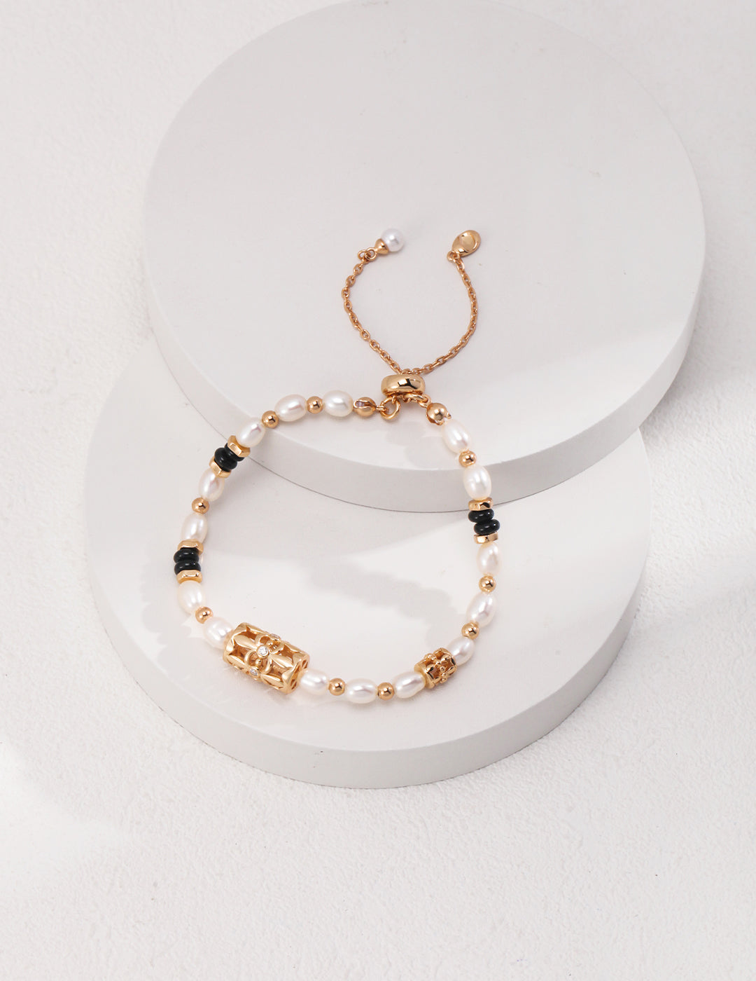 Gold bracelet with freshwater pearls, black agate, and cubic zirconia on white surface.