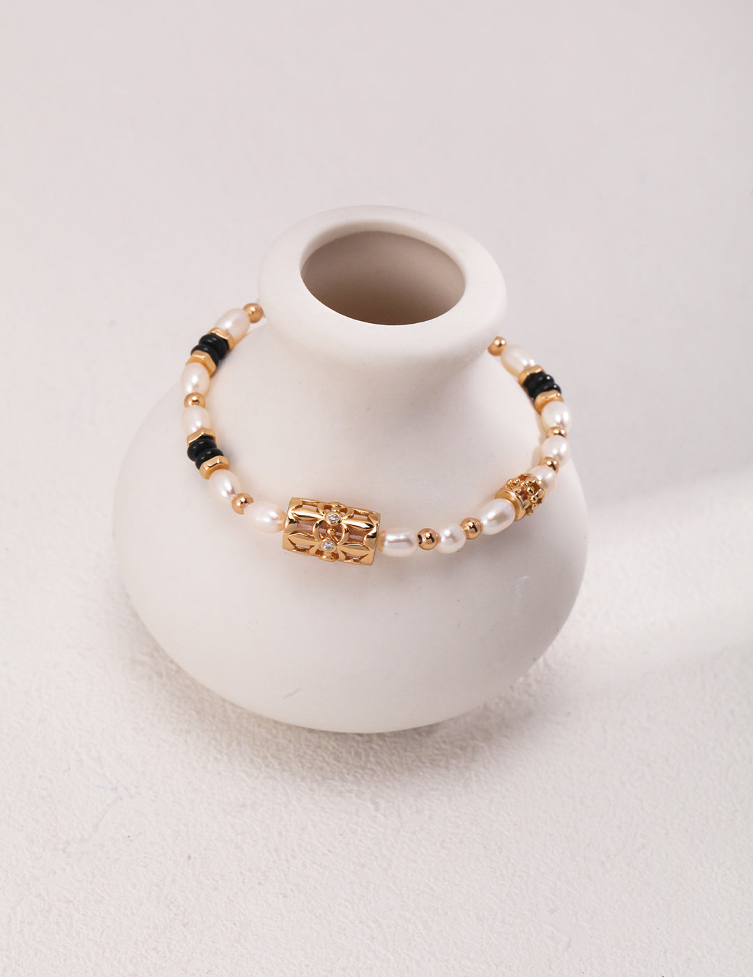 White vase with elegant gold and black bracelet adorned with freshwater pearls, black agate, and cubic zirconia.