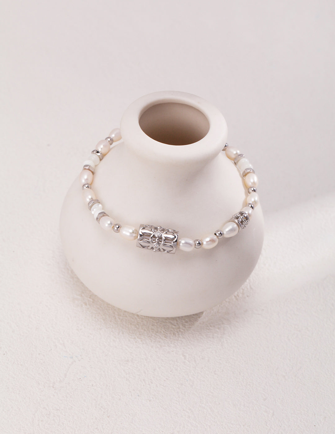 A white vase with a silver bracelet adorned with freshwater pearls and cubic zirconia on top.