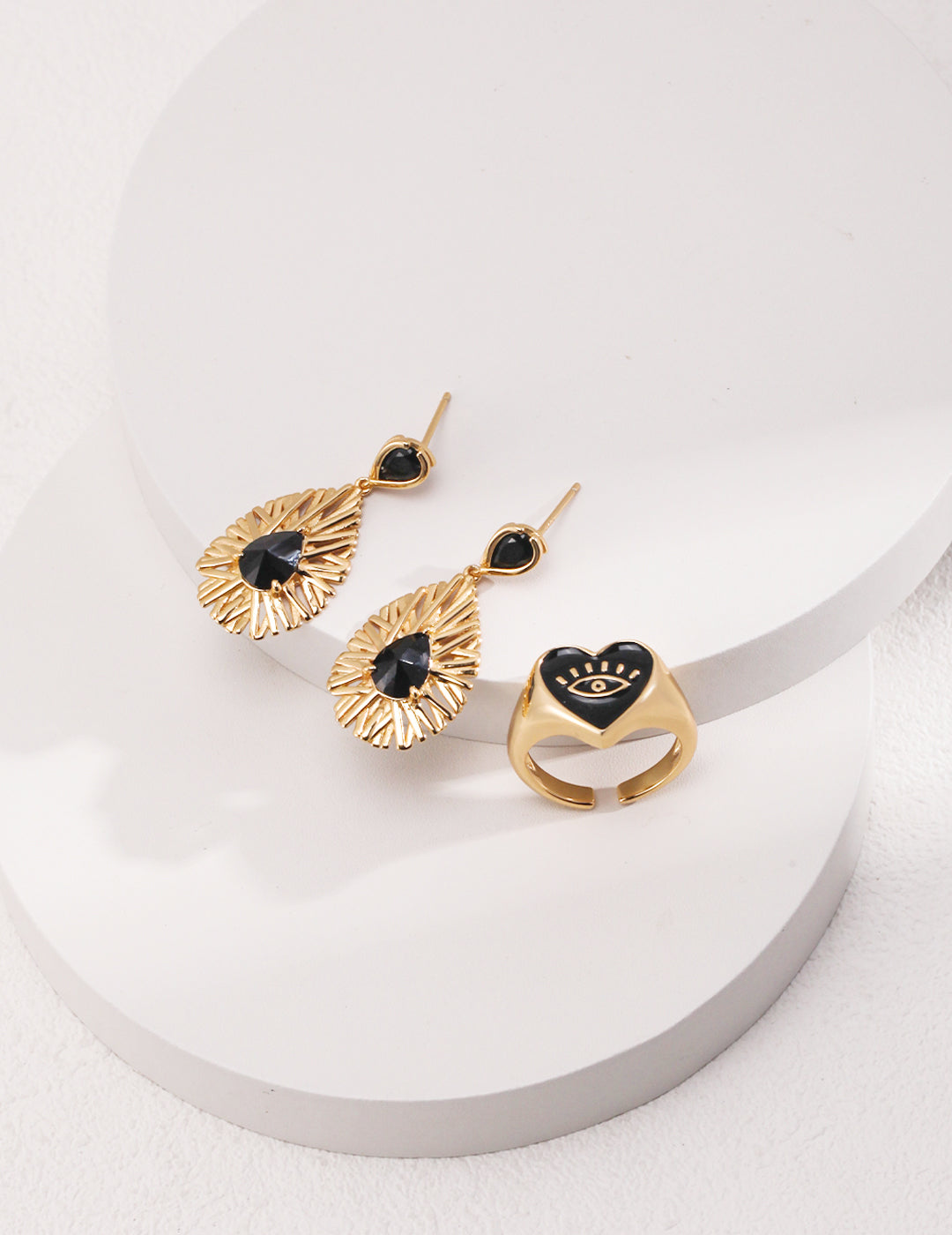 Gold heart-shaped evil eye signet ring and matching earrings in black and gold.