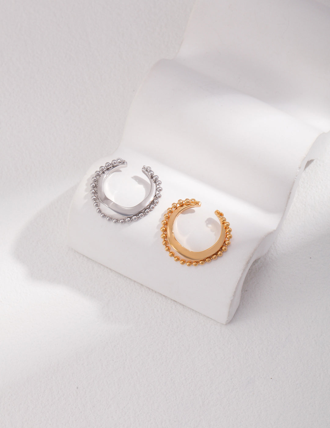 Two elegant earrings, one gold and one silver, resting on a white surface. A beautiful duo of layered silver and gold rings.