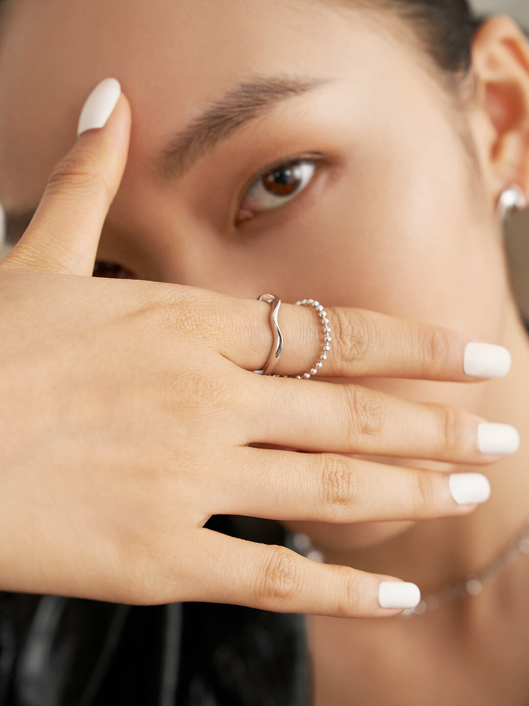 A woman's hand with white nails and a duo layered silver ring on her finger.