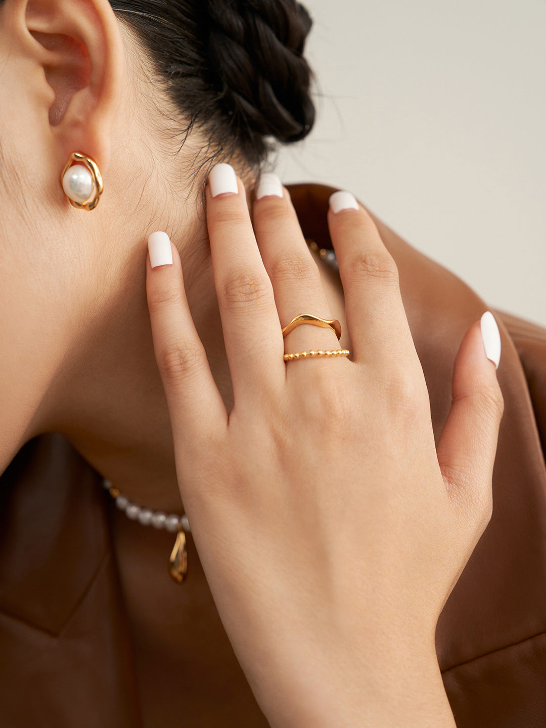 A woman wearing a gold ring and pearl earrings, showcasing a duo layered gold ring design.