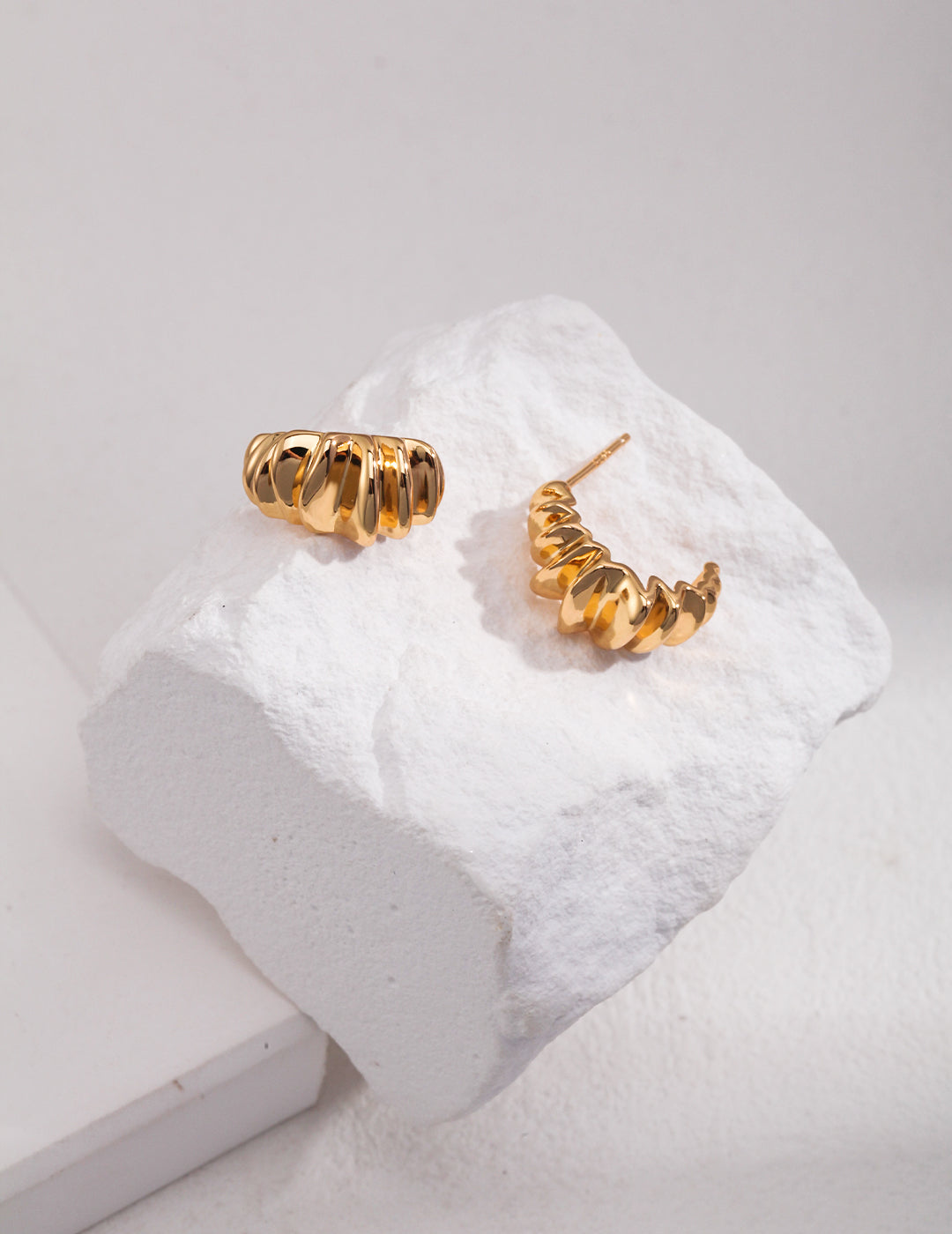 A pair of gold earrings glistening on a white rock prop, showcasing their elegance and beauty.