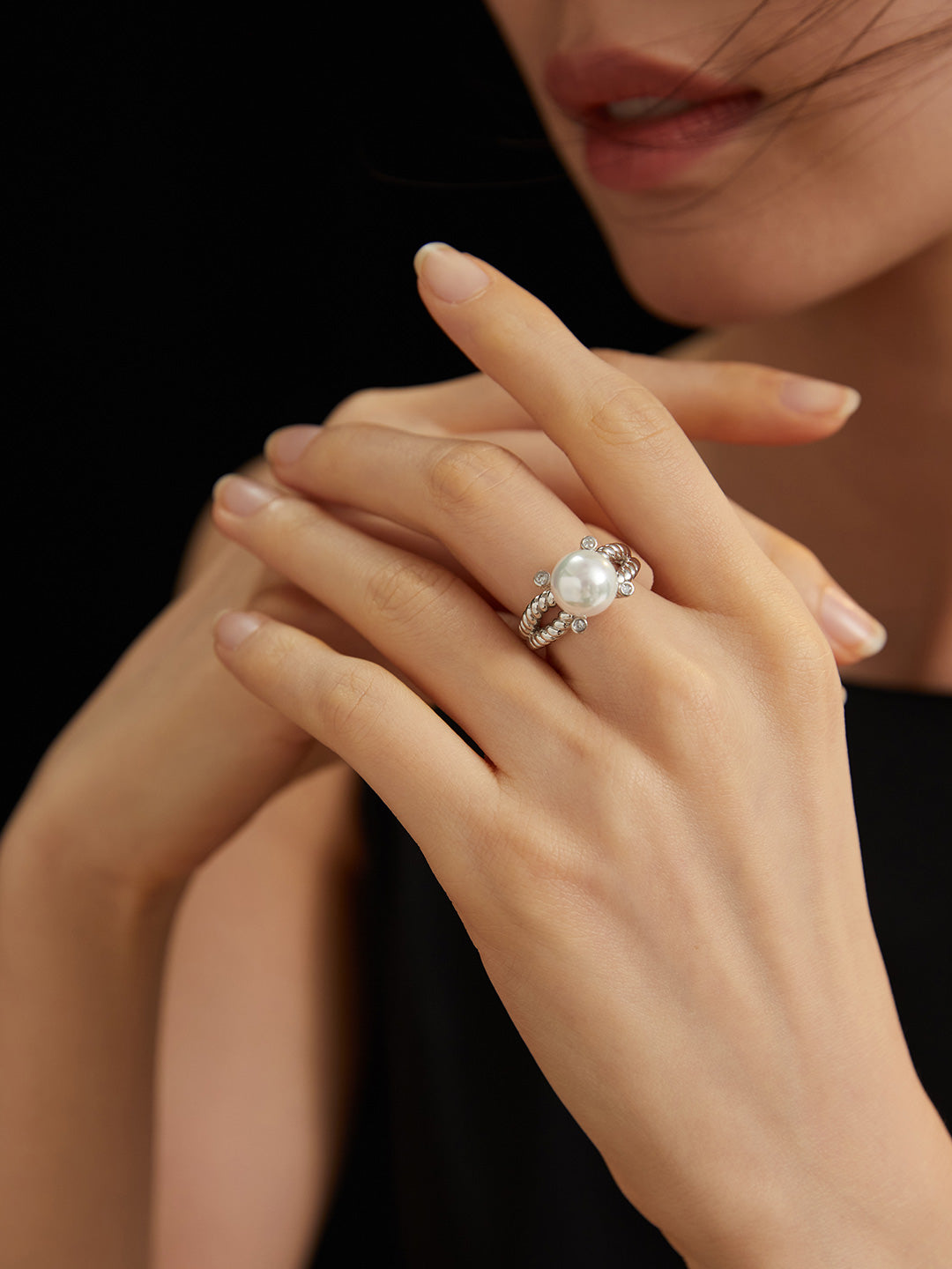 Close-up of woman's hand adorned with cubic zirconia and silver shell pearl ring.