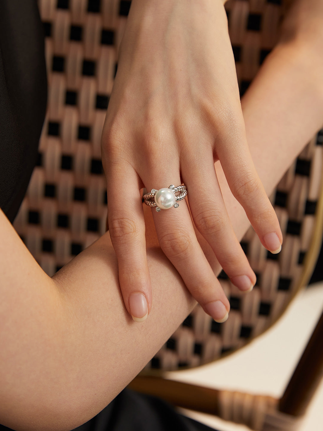 Hand showcasing silver braided band ring with shell pearl, featuring stunning cubic zirconia.