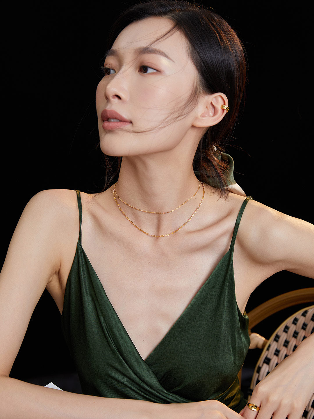 Woman in green dress on chair, accessorized with double layer gold chain necklaces.