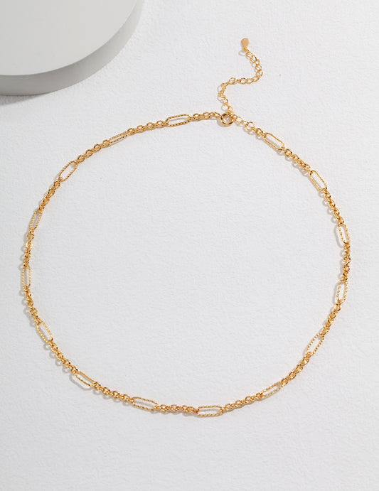 Gold chain link necklace on white surface.