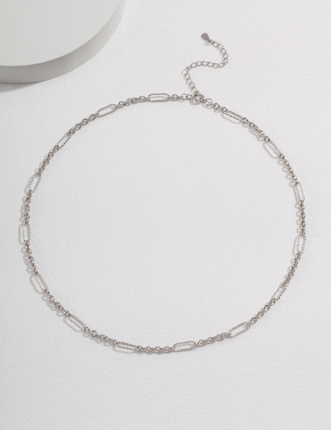 A silver chain link necklace displayed on a white surface.