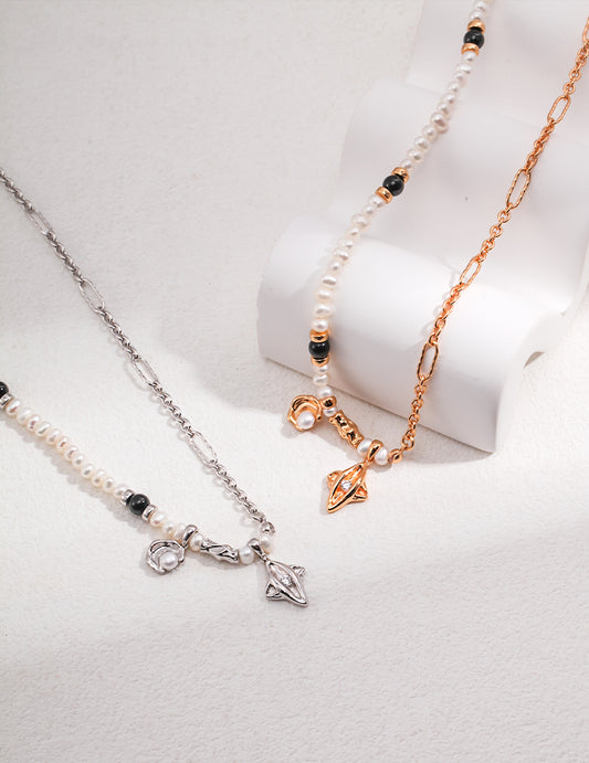 Two silver and gold chain necklaces adorned with celestial charms and freshwater pearls on a white surface.