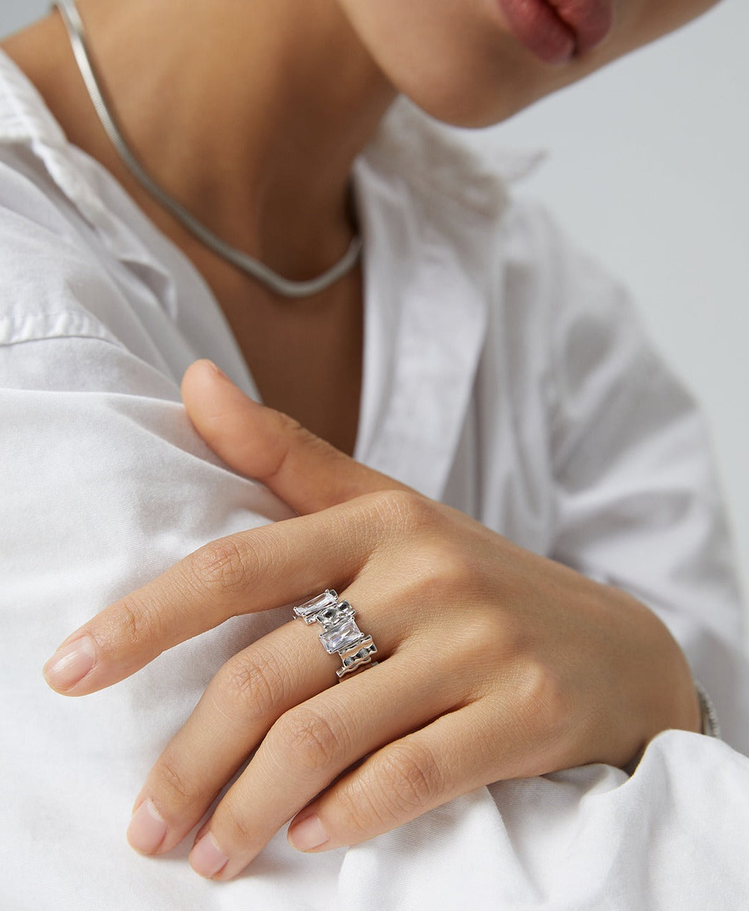 A woman in a white shirt showcasing a silver cubic zirconia ring on her finger.