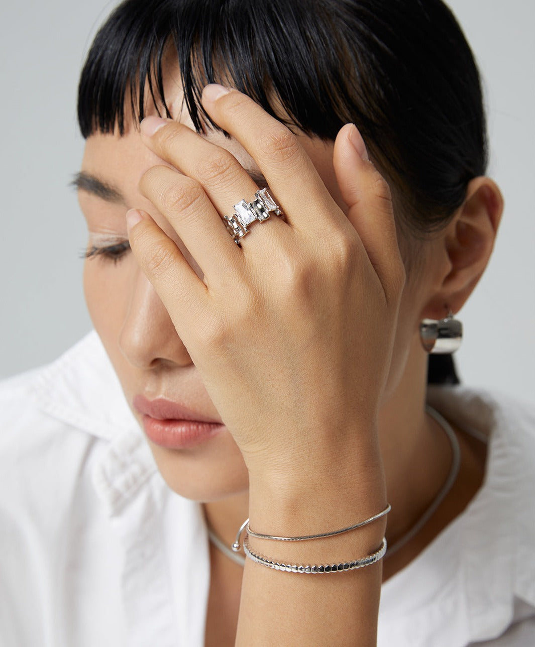 A woman wearing a white shirt and a silver cubic zirconia ring on her hand.