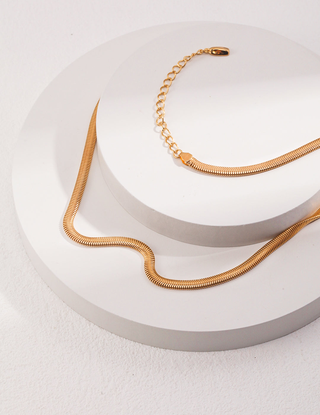 A gold snake chain necklace displayed on a white plate.