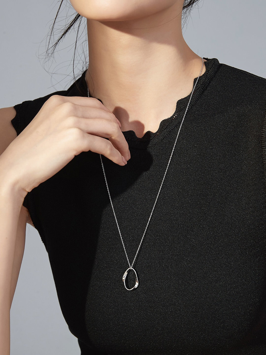 Female in black shirt accessorized with silver chain necklace, oval design.