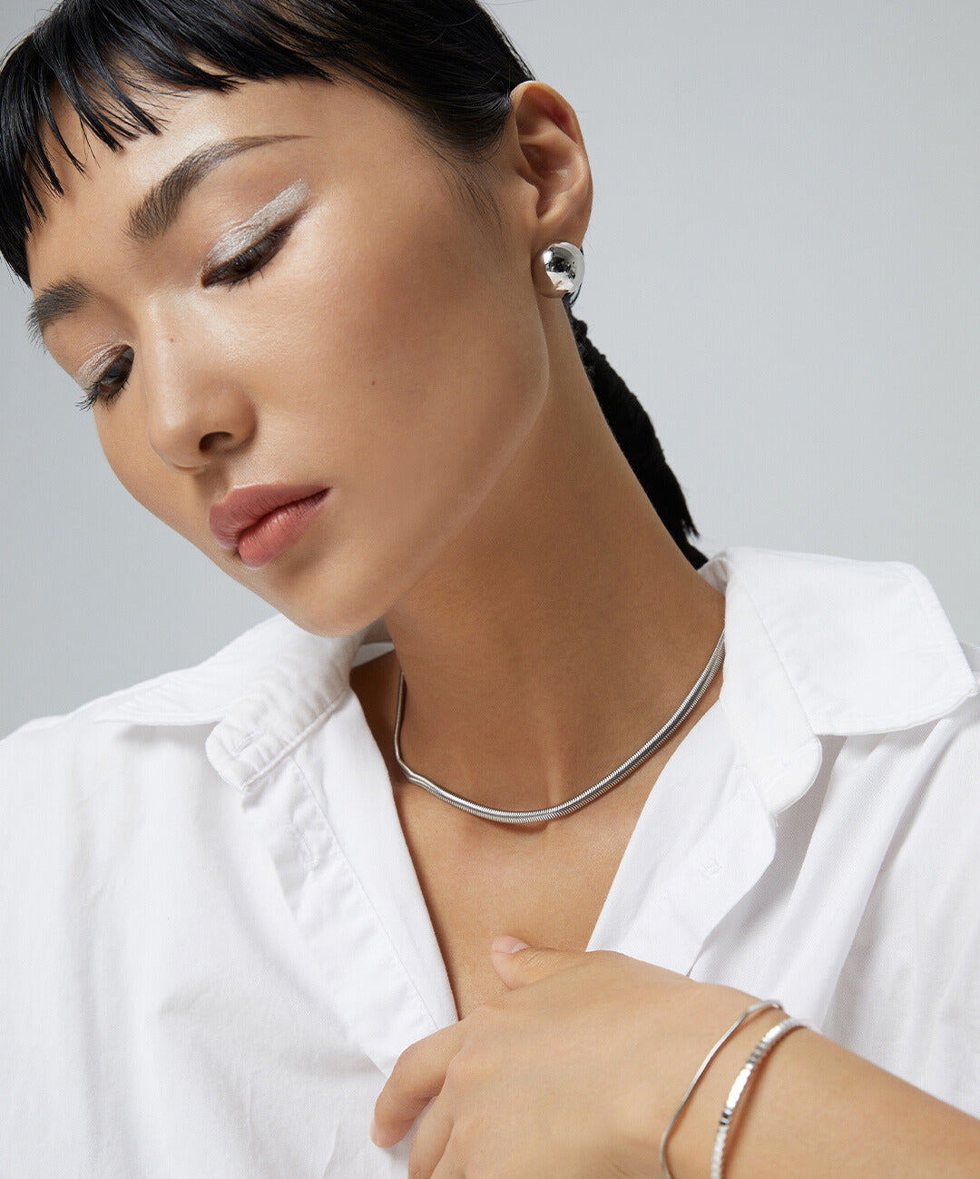 Model showcasing white shirt and silver jewelry, featuring snake chain necklace.