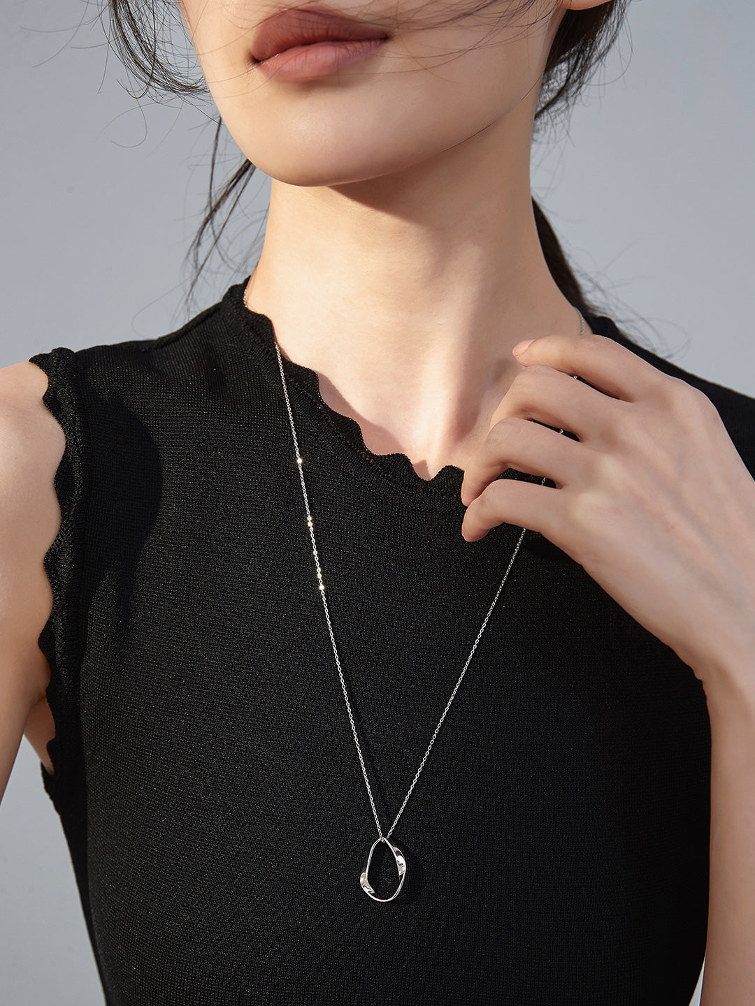 A woman in a black top wearing a silver necklace with a hollow oval shape pendant.