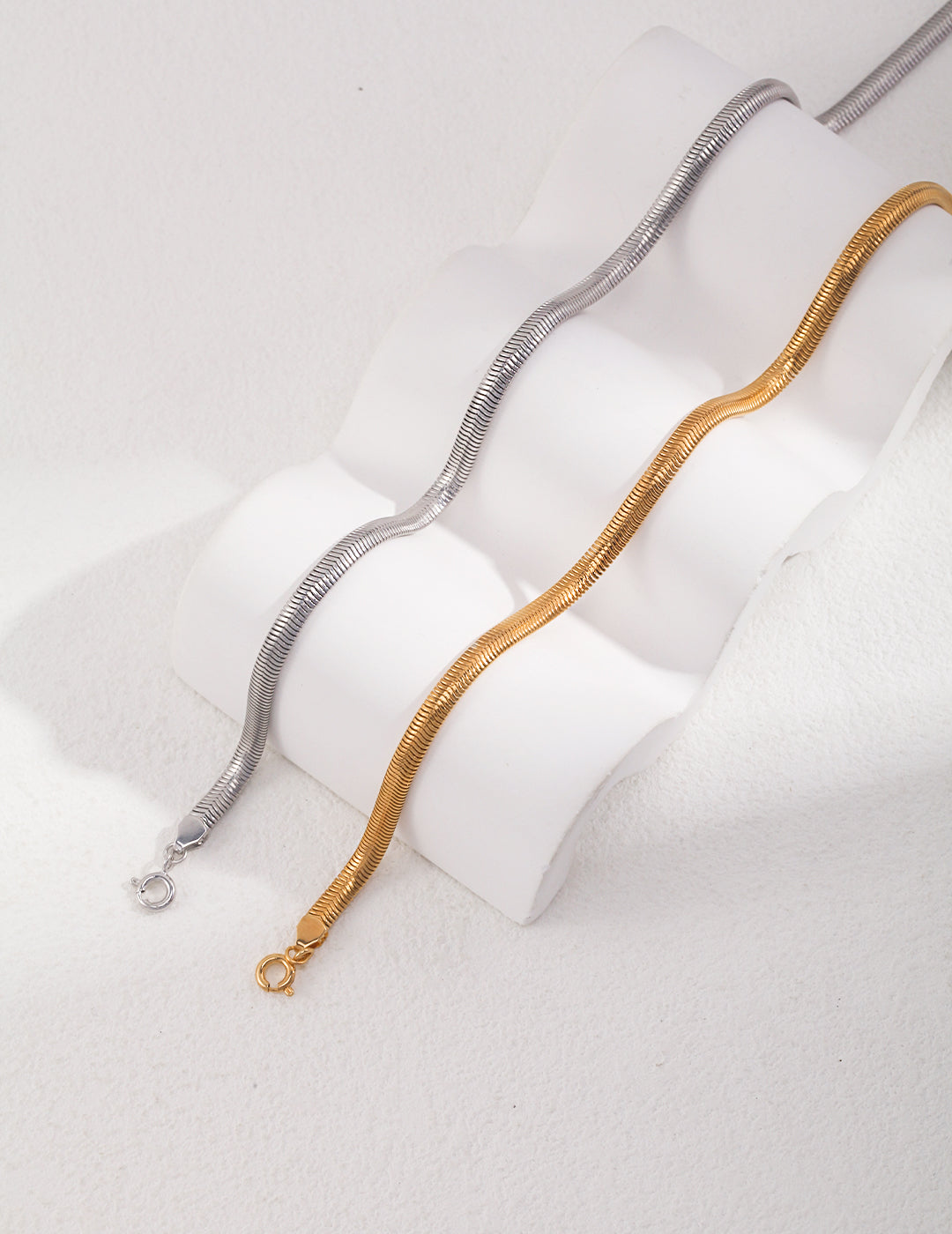 Silver and gold snake chain necklaces resting on white surface.