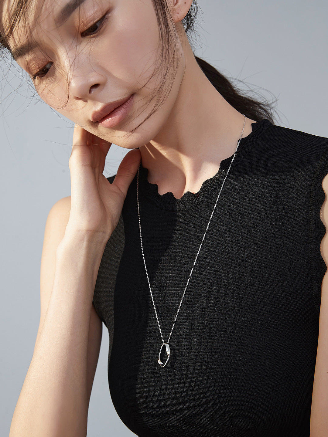 Black top-clad woman donning silver chain necklace with oval pendant.