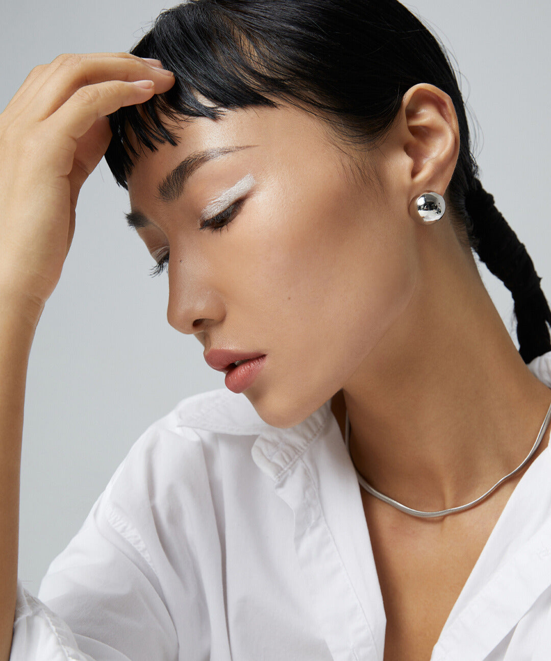 Model in white shirt, hair pulled back, accessorized with silver snake chain necklace.