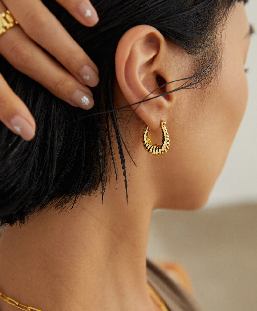 A woman wearing gold twisted hoop earrings and a matching gold chain.