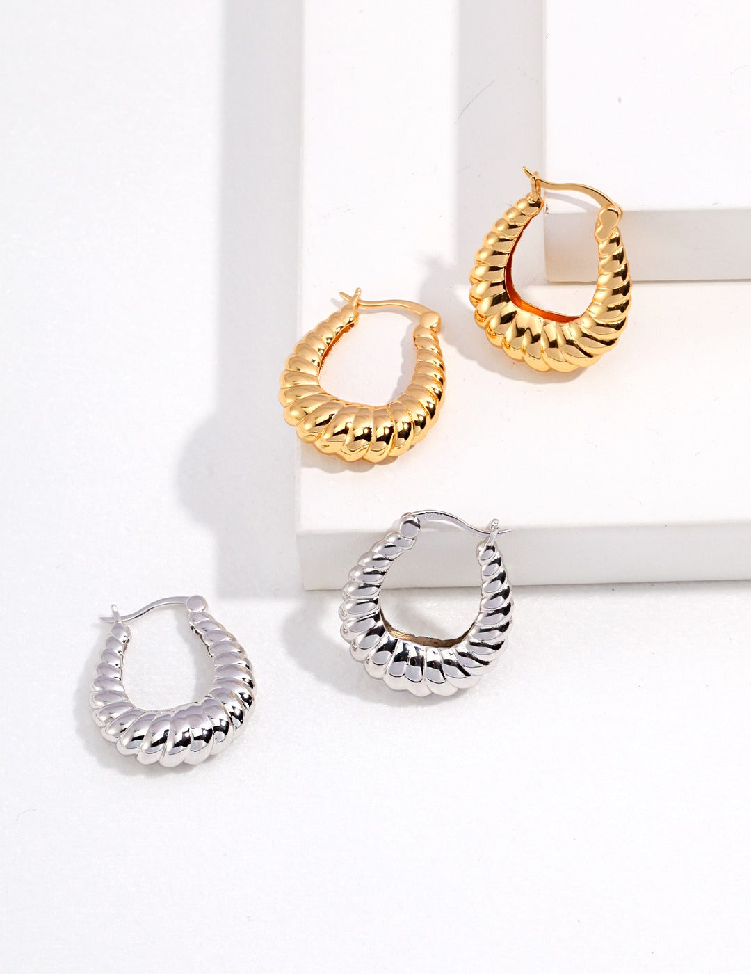 Two pair of twisted hoop earrings: one silver, one gold on a white surface.