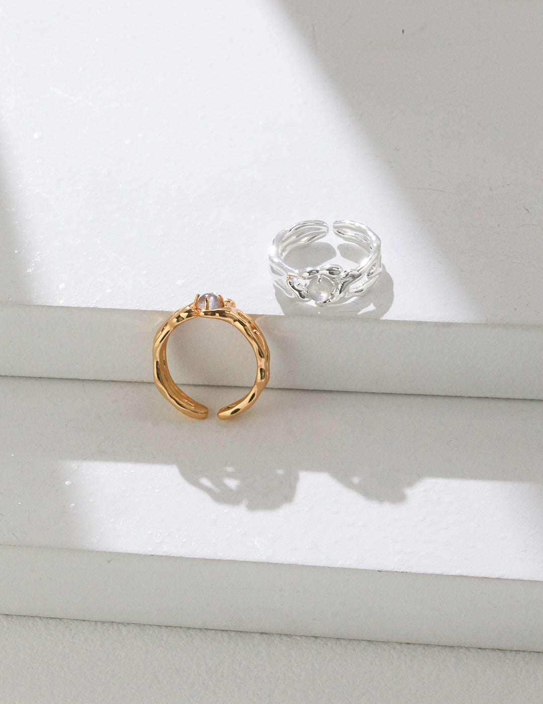 Two labradorite rings, one silver and one gold, resting on a white surface.