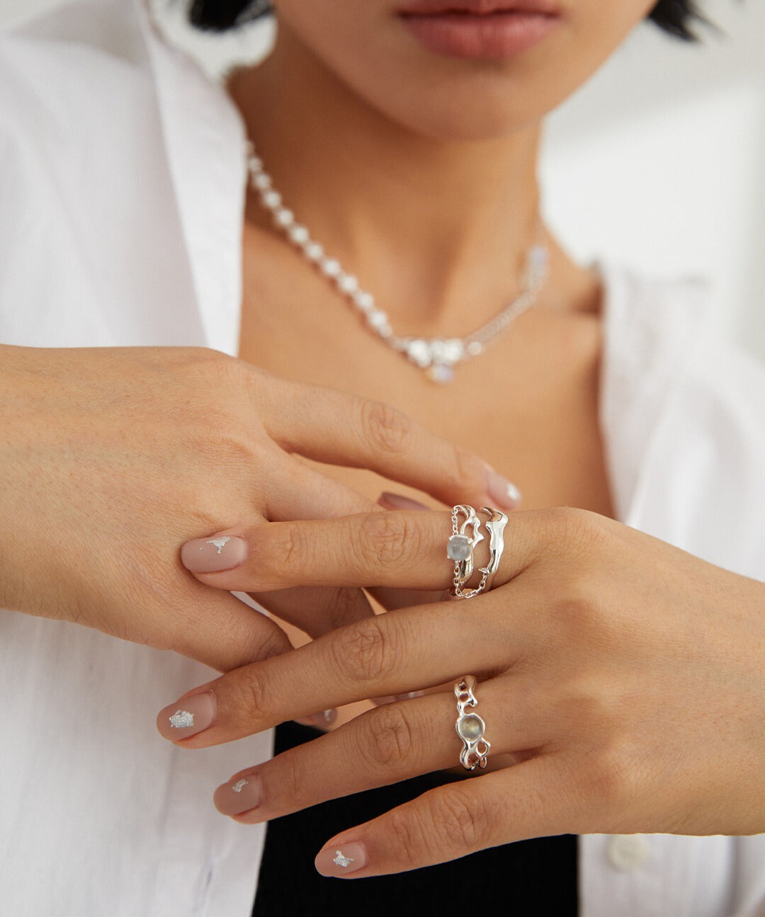 A woman wearing a white shirt and silver jewelry, showcasing a silver plated labradorite ring.