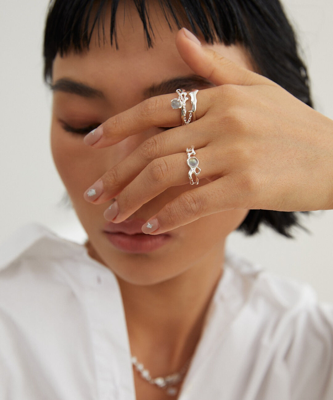 A woman in a white shirt wearing silver plated labradorite rings.