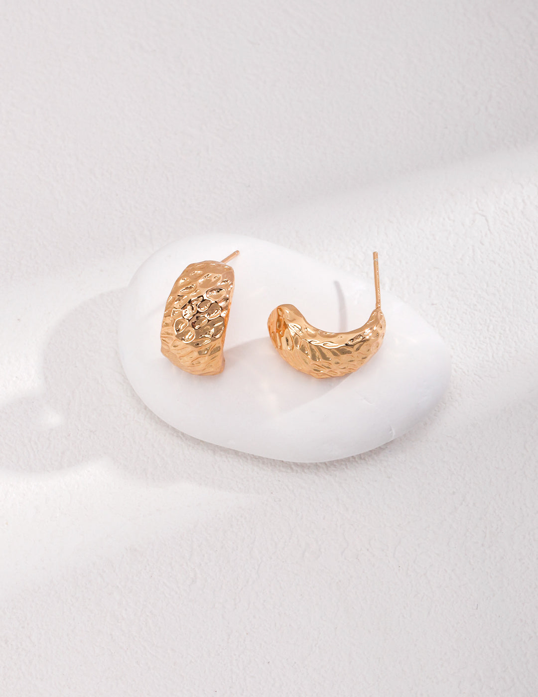 Shimmering gold earrings elegantly displayed on a pristine white background.