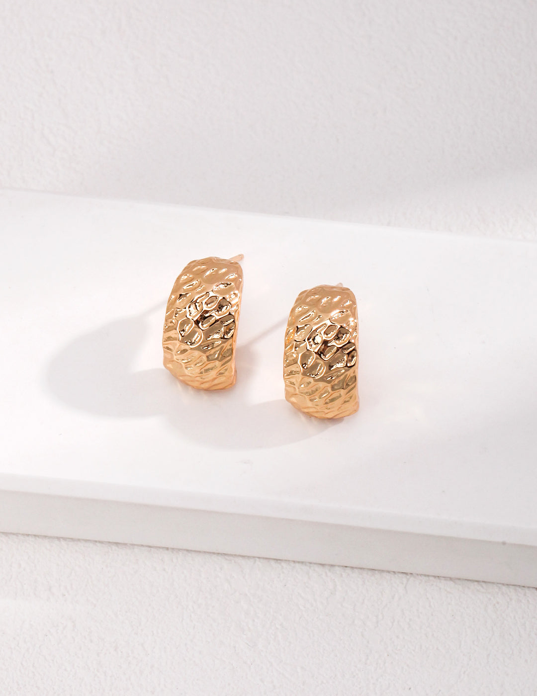 Gold plated earrings on a white tray.
