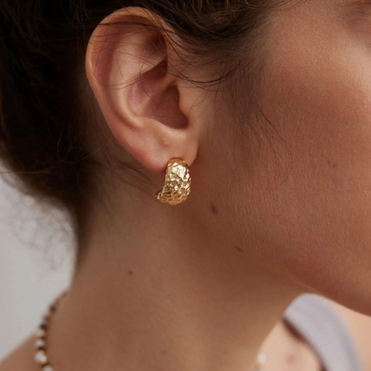 A woman with textured gold earrings and a gold necklace, emphasizing her chic and stylish appearance.