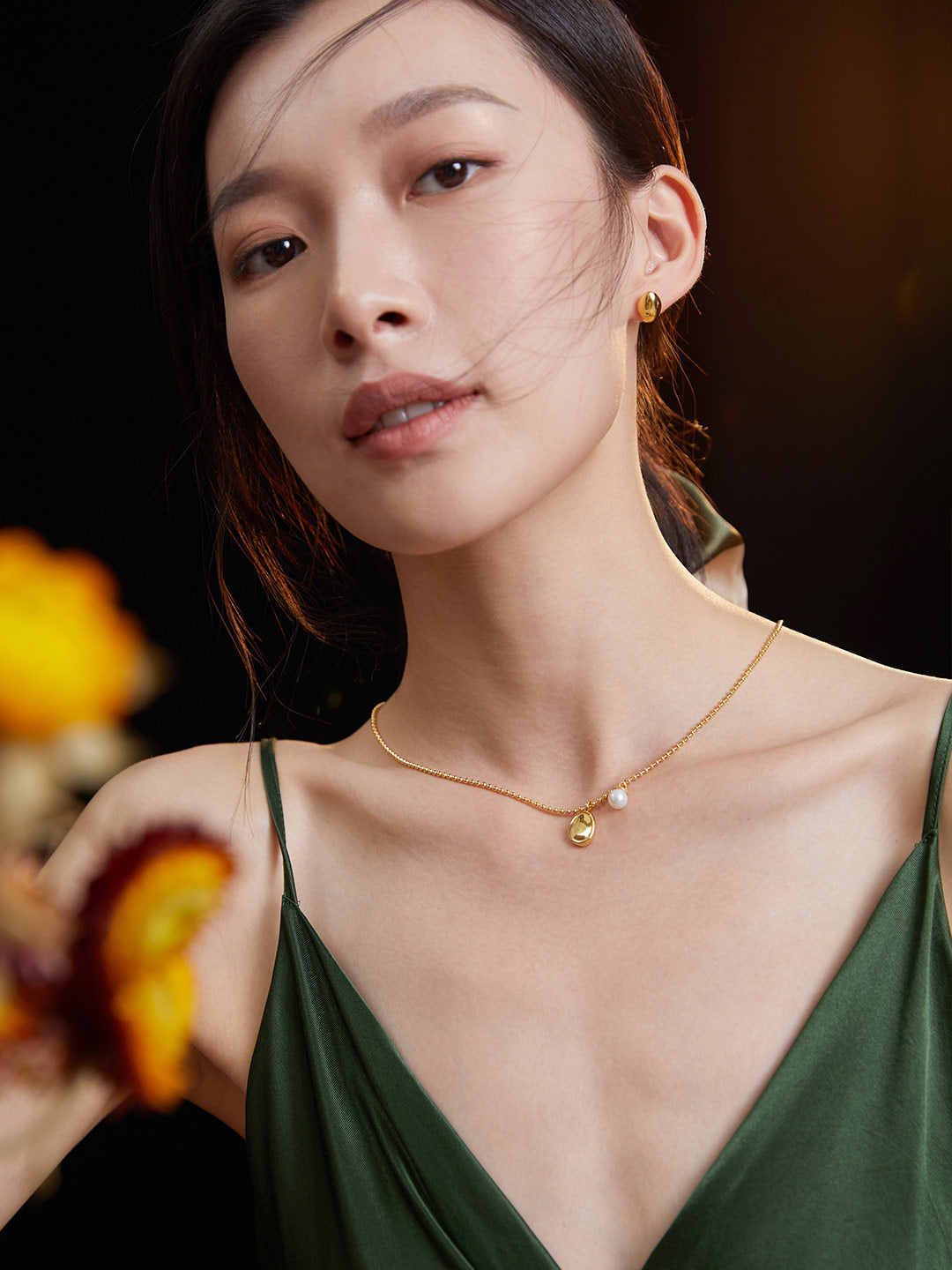  Lady in green dress with flower, accessorized with gold chain necklace and bean pendant.