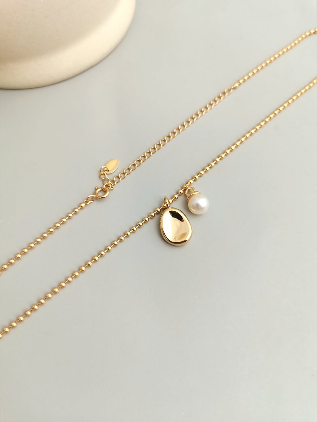 Close up shot of gold chain necklace with pearl and small bean pendant.