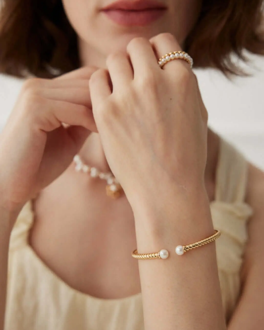 A close-up of a woman’s wrist featuring a contemporary gold bangle with a pearl accent.