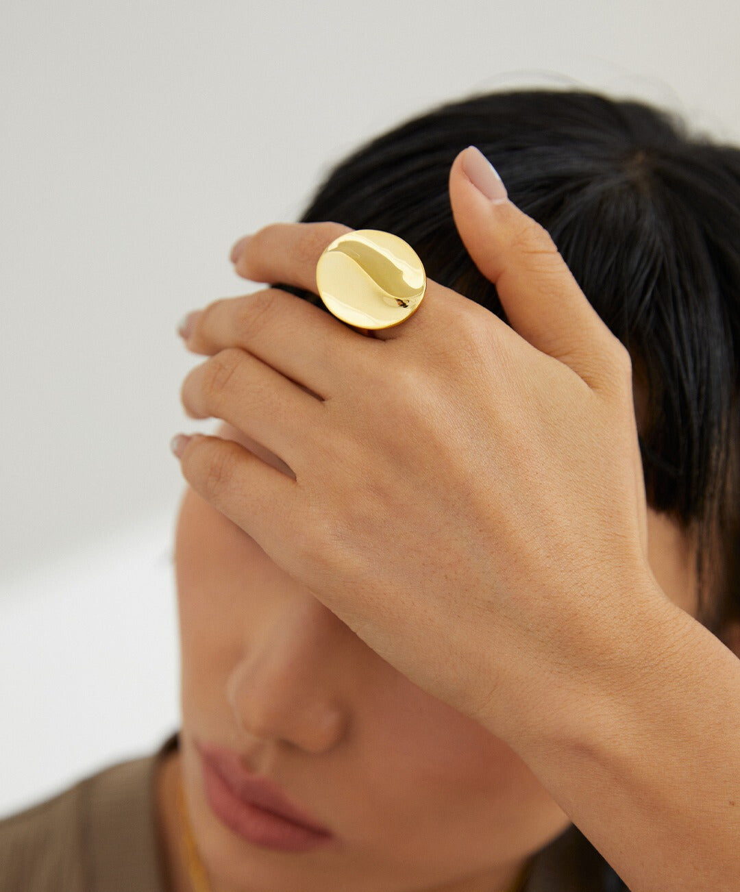 Woman placing hand over head, wearing a gold coffee bean ring.