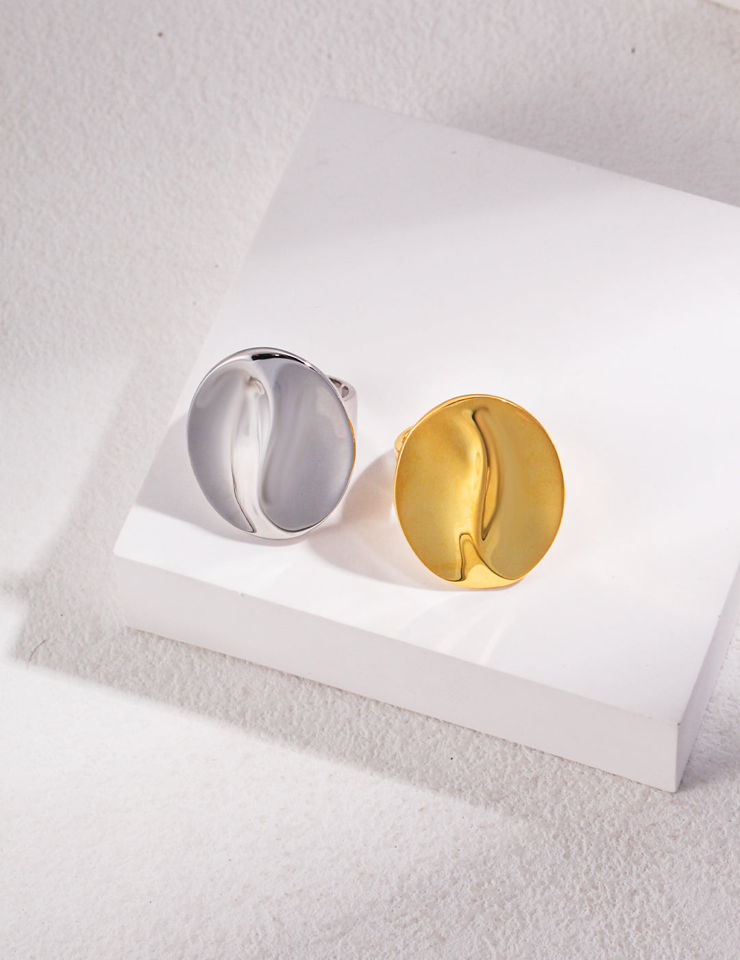 Two coffee bean inspired rings, one gold and one silver, placed on a white surface.