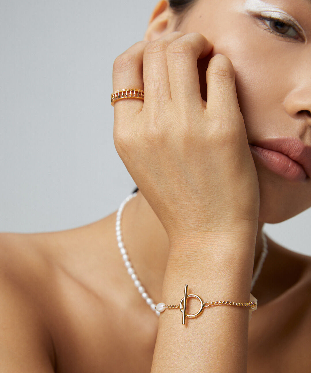 A woman wearing a pearl and gold bracelet, along with other matching jewelry, featuring freshwater pearls.