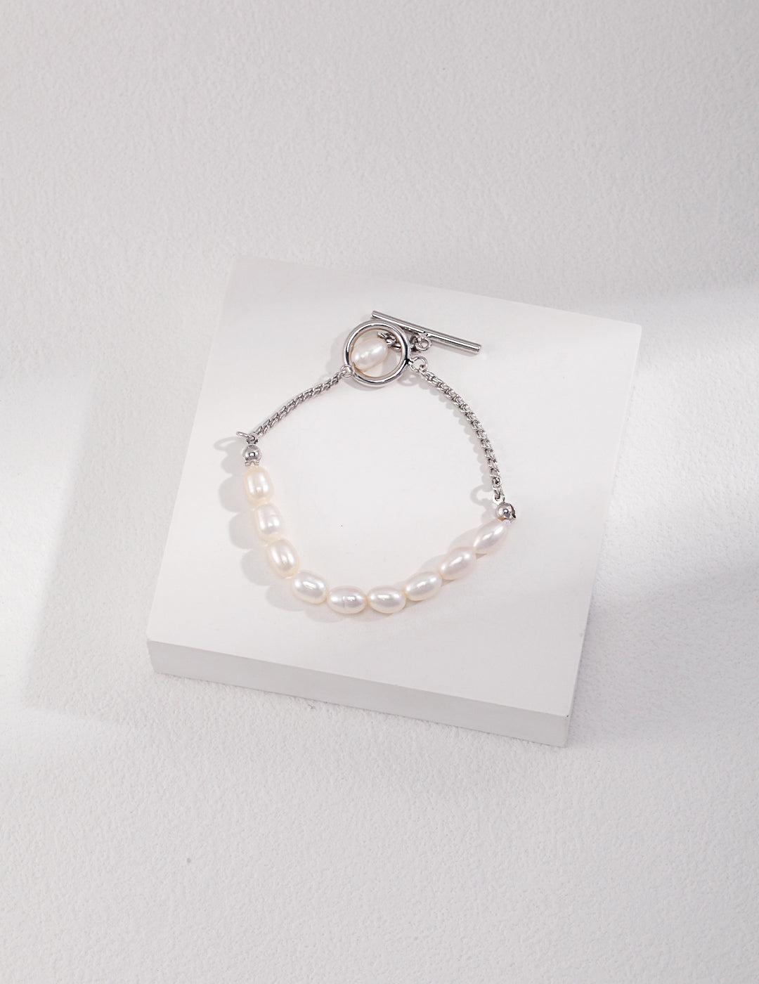 Elegant white freshwater pearls bracelet with silver chain, resting on white surface.