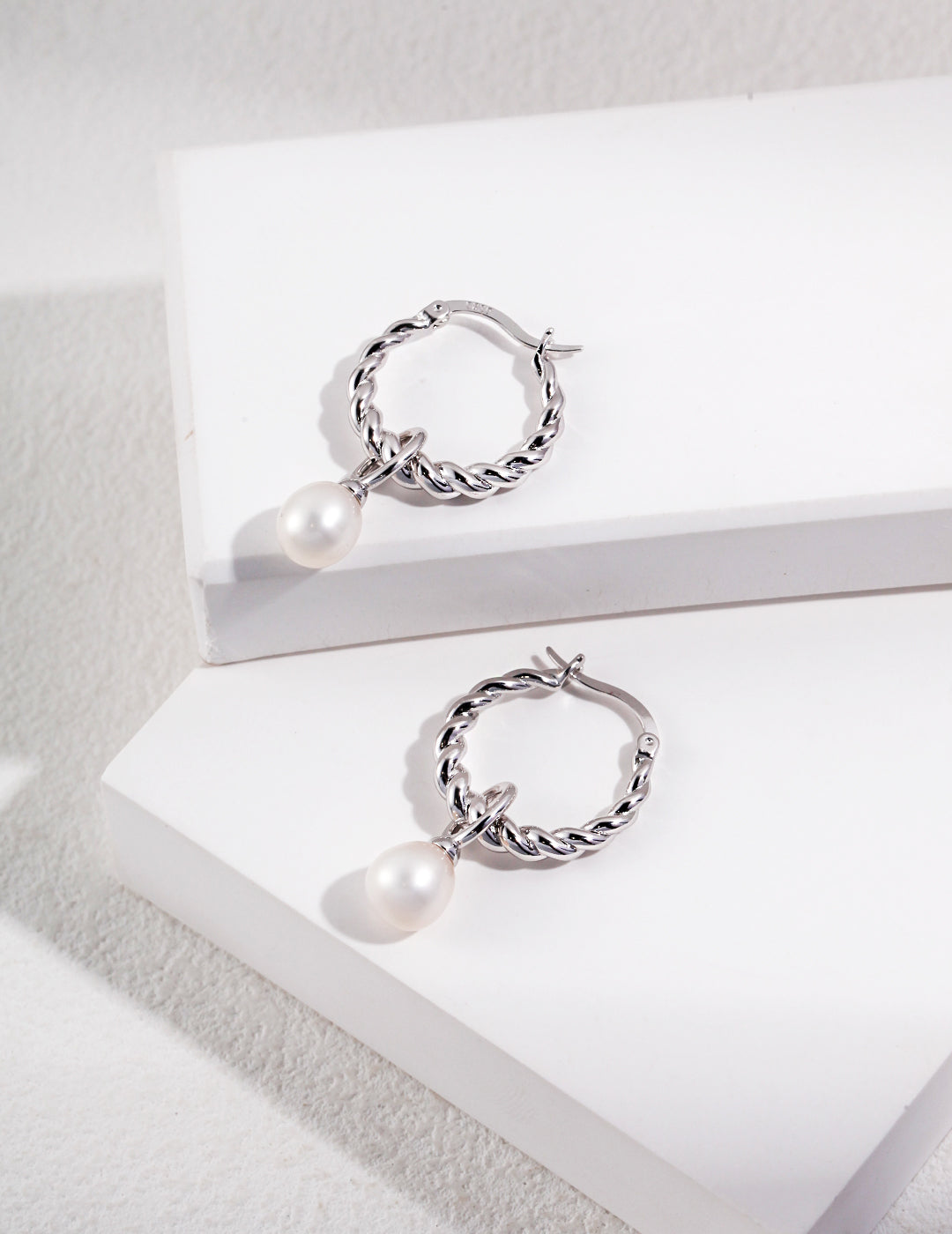 A pair of freshwater pearl hoop earrings on white box, elegant silver accents.