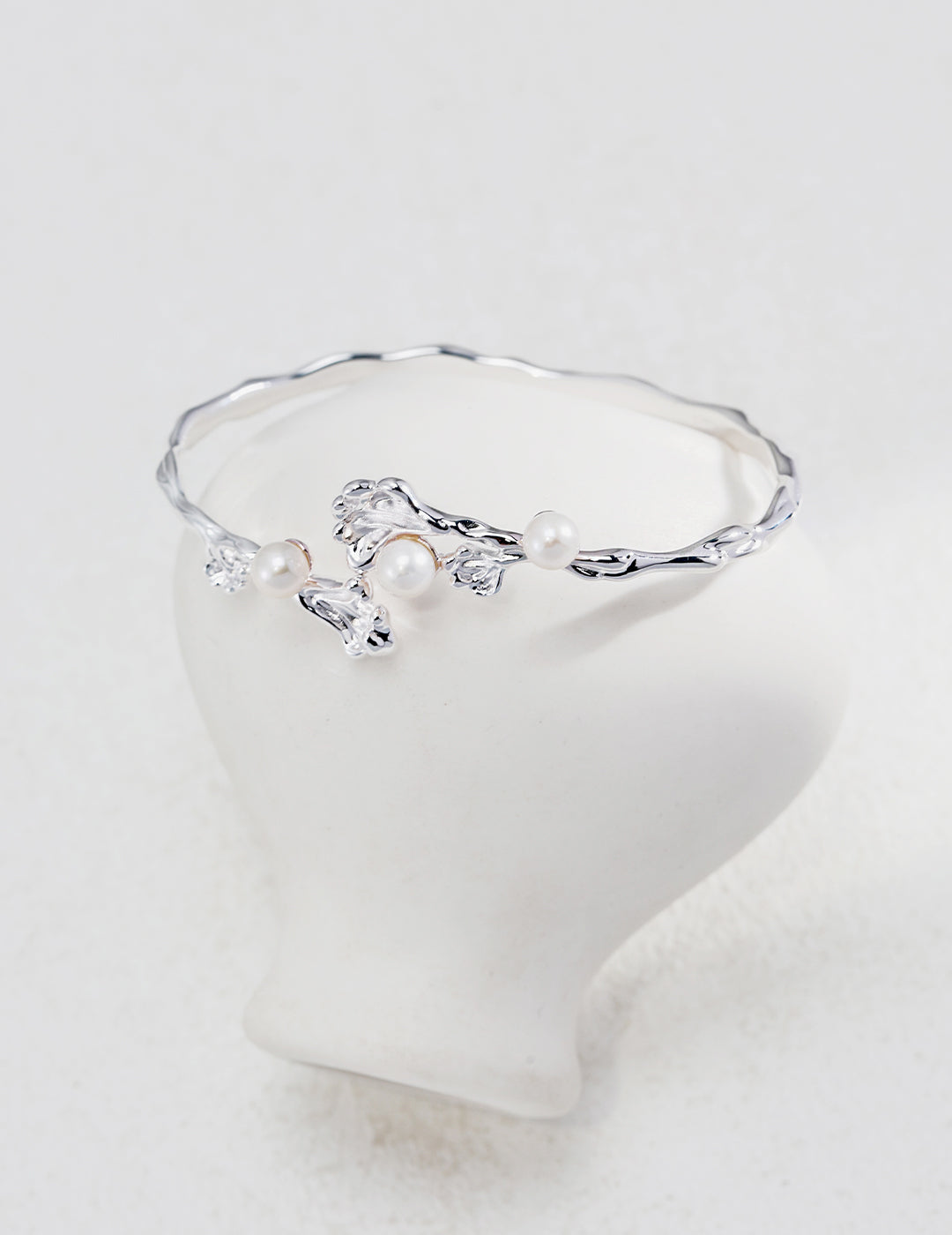 A stunning silver bangle with freshwater pearls and diamonds, resting on a white inverted vase.