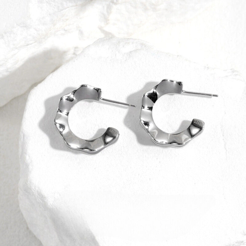 Elegant silver hoop earrings with ripples on white stone.