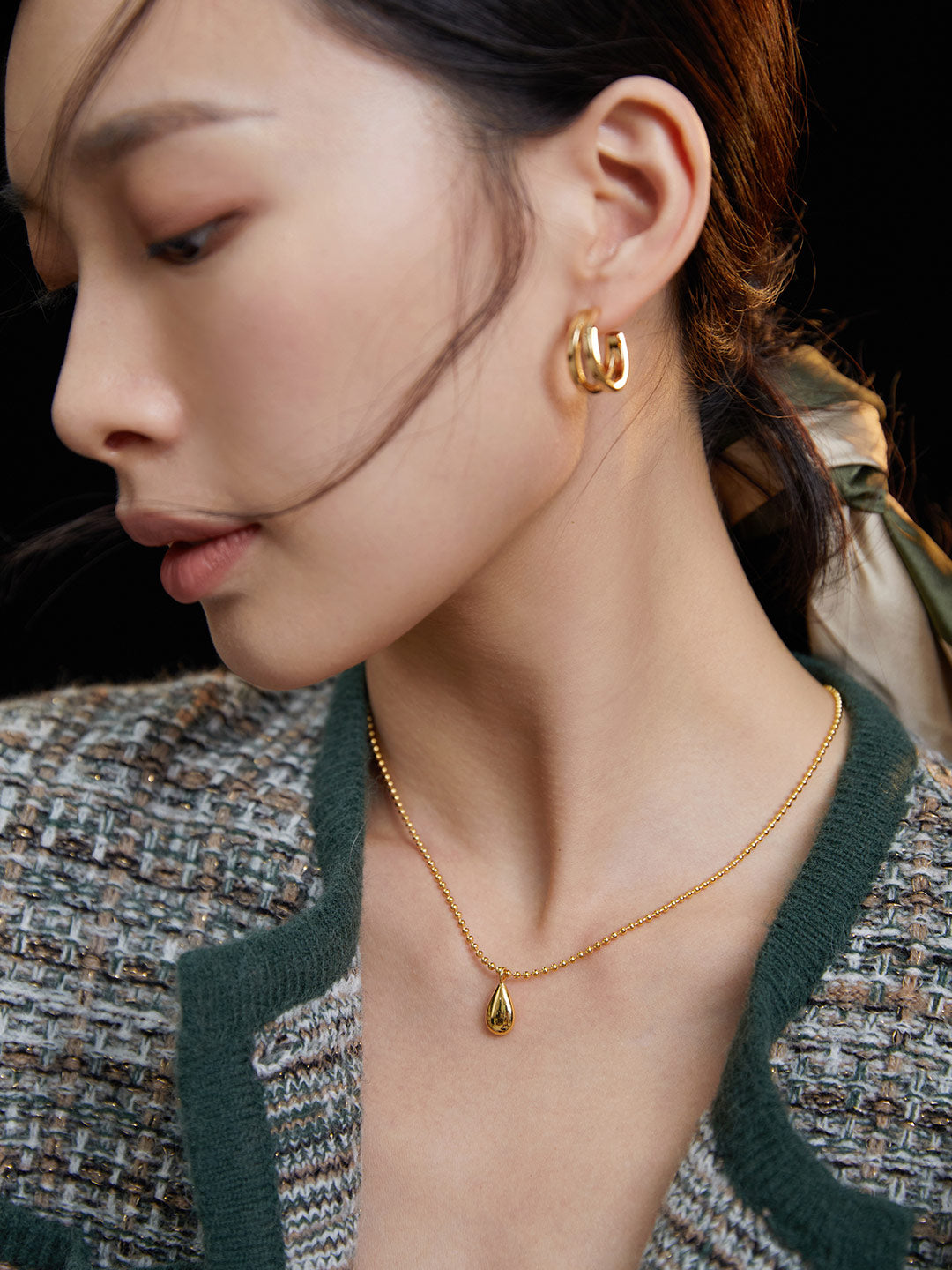 A woman showcasing her elegance with a gold teardrop necklace and matching earrings.