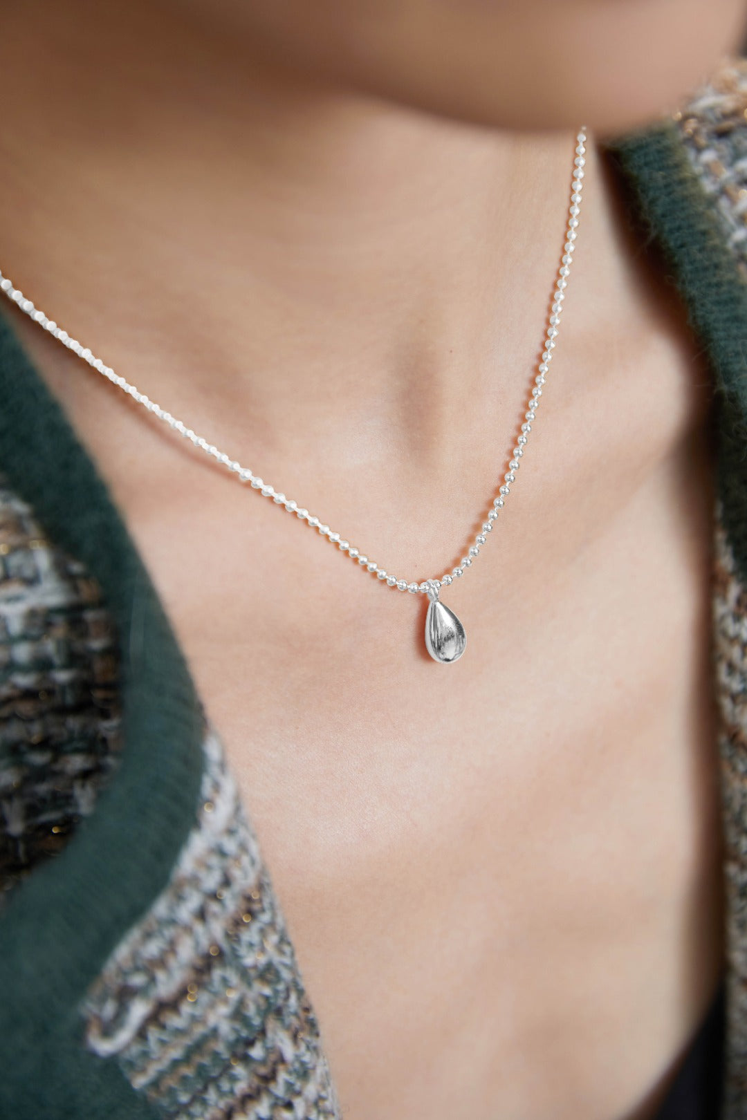 Silver necklace with teardrop stone worn by stylish woman.