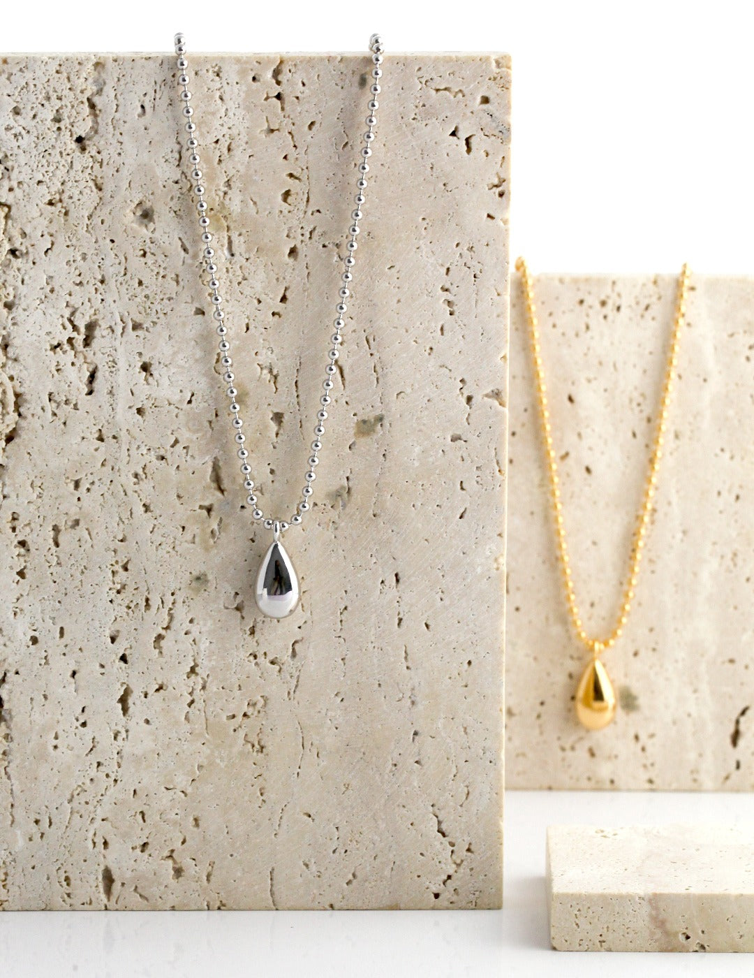 Two teardrop necklaces, one in silver and one in gold.