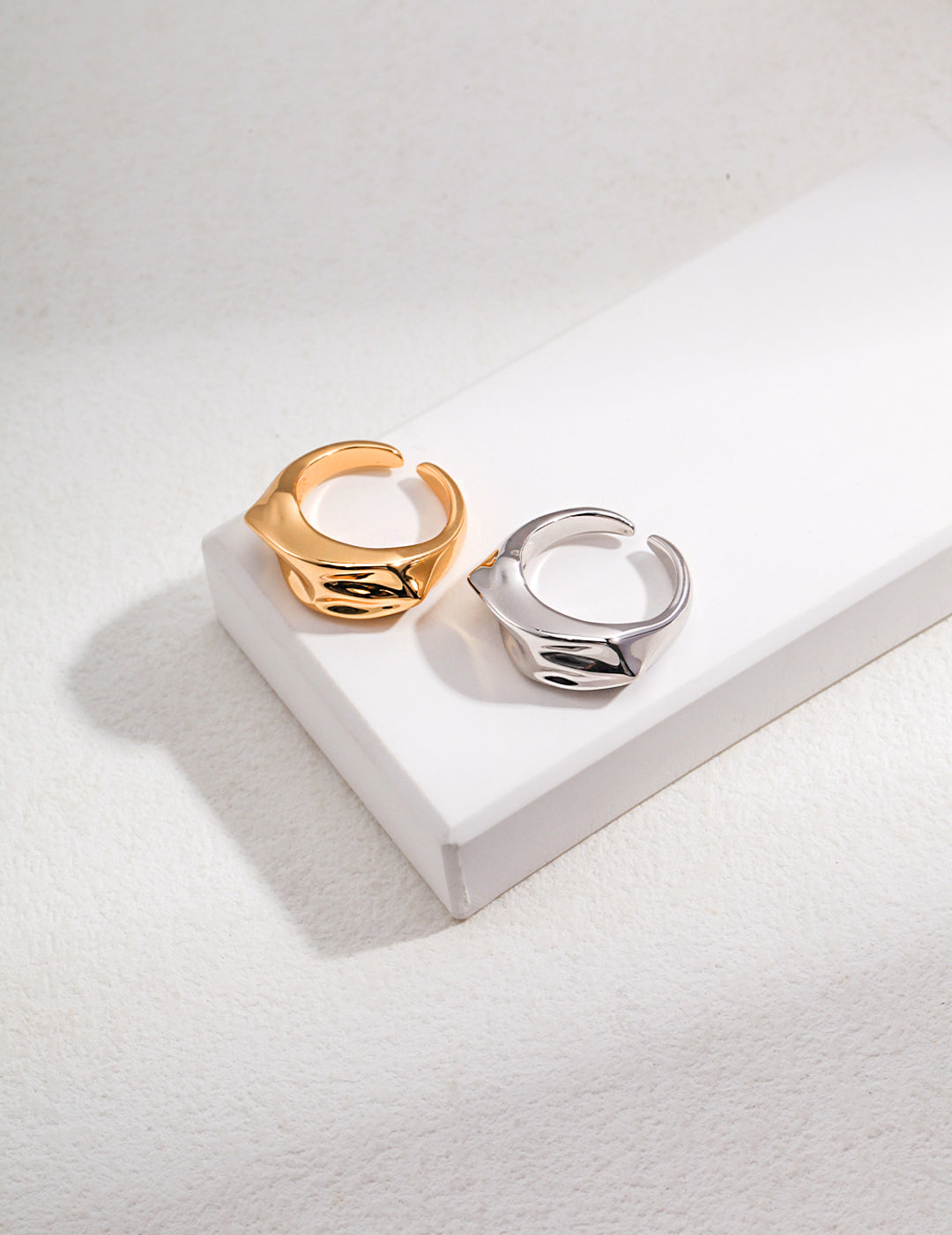 Two wavy design rings, one gold and one silver, placed on top of a white box.