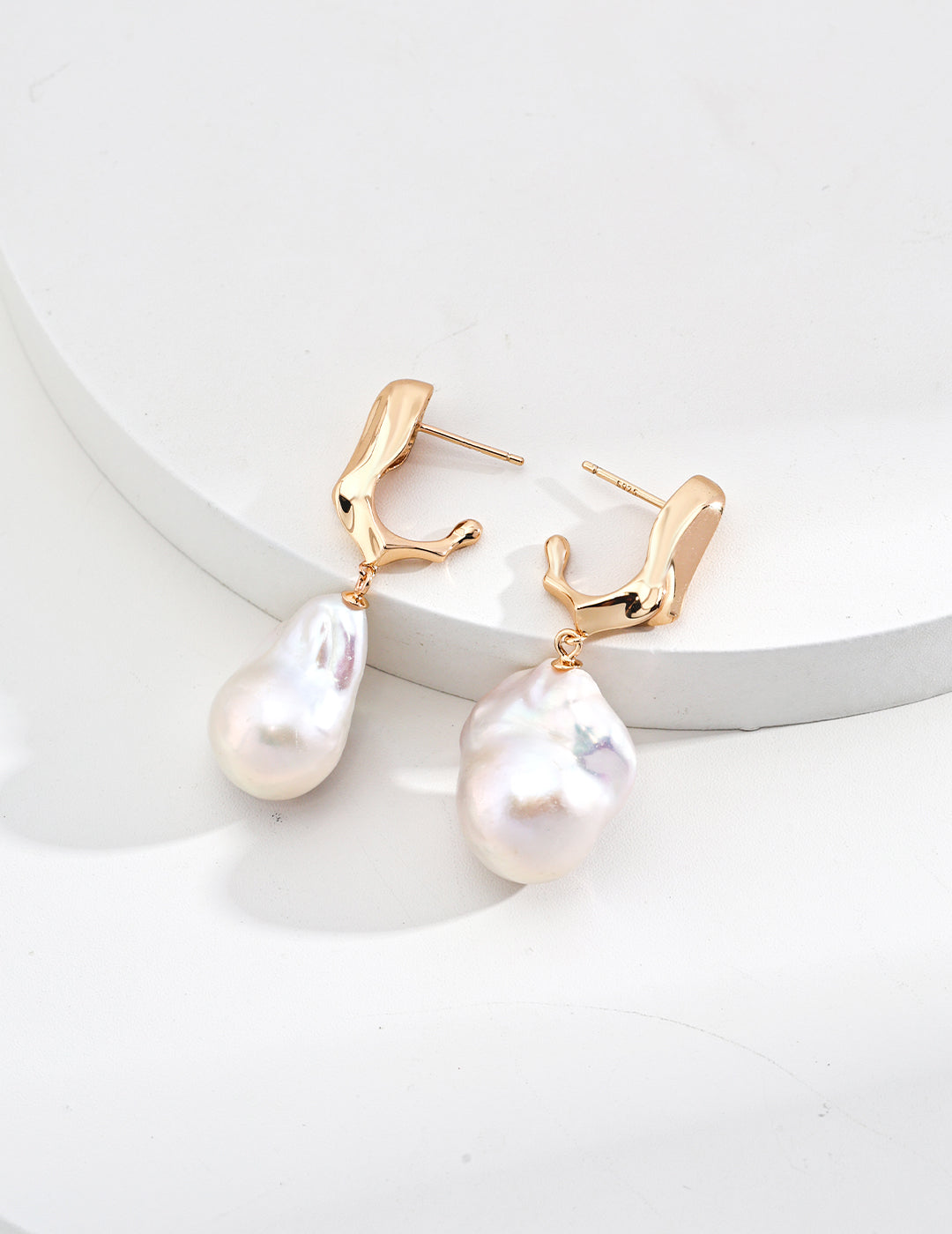 A close-up product photograph of the 18K gold-plated Genevieve earrings, highlighting their organic molten-textured settings and suspended natural freshwater baroque pearls.