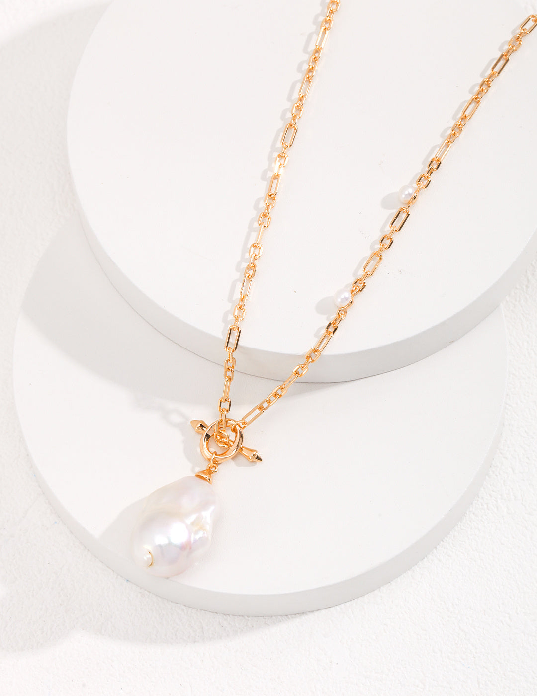 A product photograph of the 18K gold-plated Anastasia necklace, showcasing its structural link chain, subtle accent pearls, and statement baroque pearl toggle pendant.