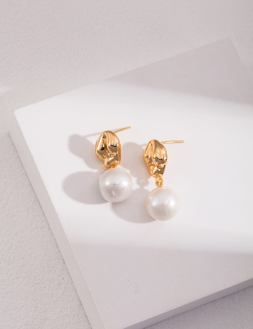 Delicate gold-plated pearl earrings showcased on a clean white surface.